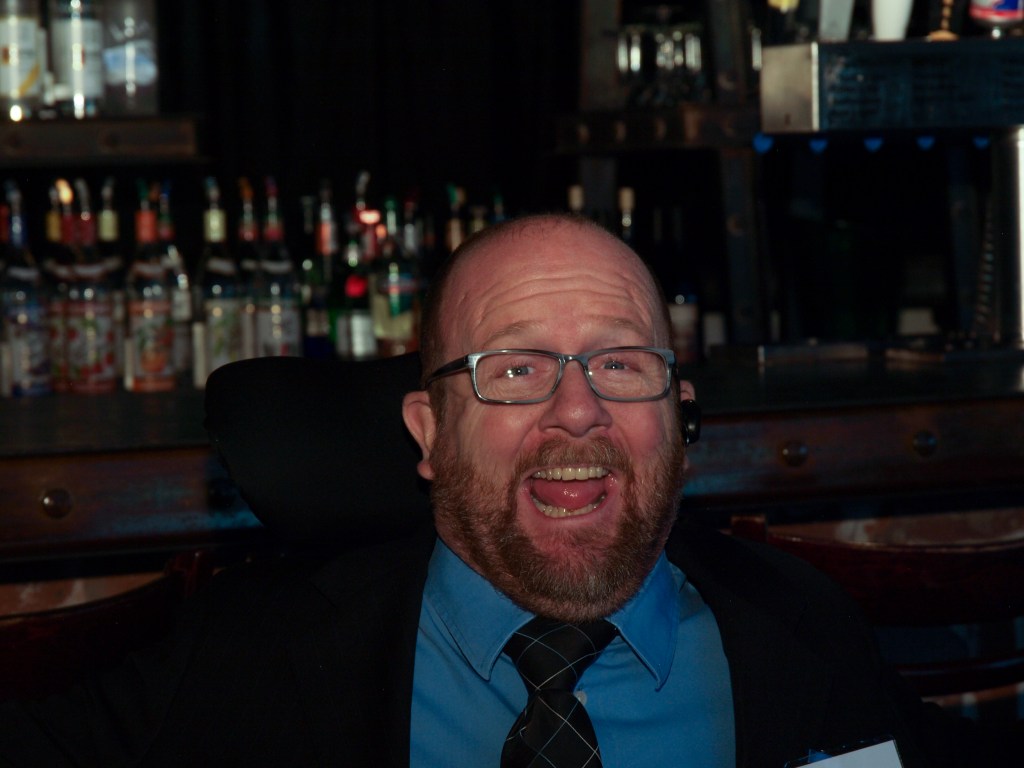 Kevin at a CCDC event, mugging for the camera with a bar full of liquor bottles in the background.