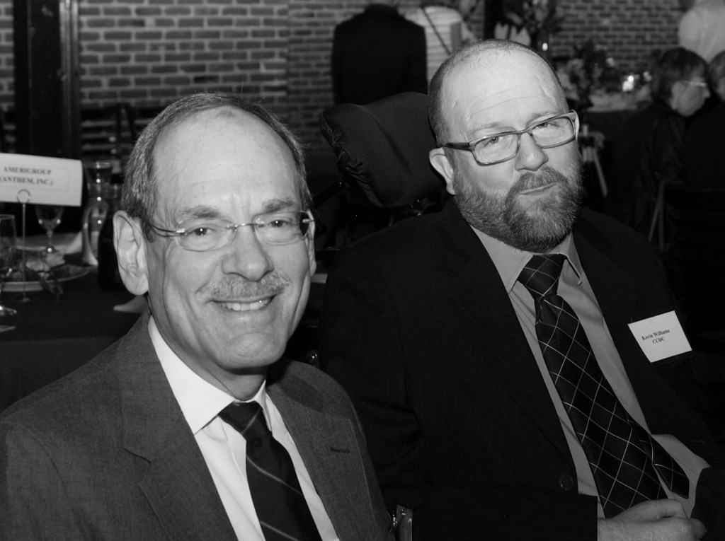 Black & white photo of Michael Breeskin (white man; glasses; mustache; suit & tie) and Kevin (suit & tie).